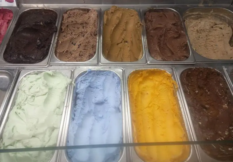 آبمیوه و بستنی بوزلی: ویترین پر از بستنی‌های سنتی و میوه‌ای با طعم‌های متنوع مانند شکلات، پسته، انبه، وانیل و بلوبری.