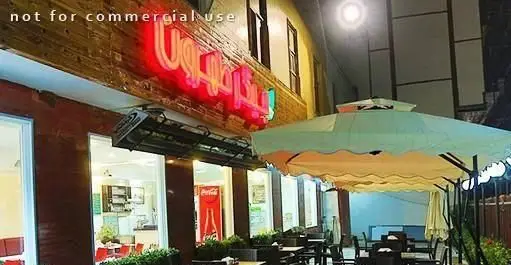 نمای شب کبابی جیگر طهرون با تابلوی نئونی روشن و فضای باز دلنشین با چتر و میز و صندلی‌ها، محیطی مناسب برای تجربه غذای ایرانی در تهرون.