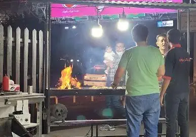 تصویری جذاب از کبابی جیگر طهرون در شب، جایی که کباب و جگر تازه با شعله‌های پرحرارت آتش و دود پخته می‌شود و مردم اطراف آن جمع شده‌اند.