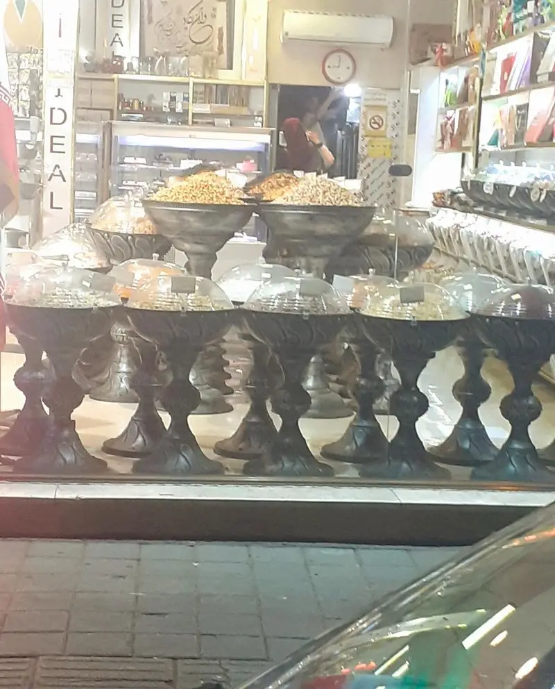 تصویری از ویترین شیرینی و آجیل فروشی ایده آل، نمایشگر آجیل های تازه و خوشمزه از جمله پسته و بادام در کاسه های بزرگ.
