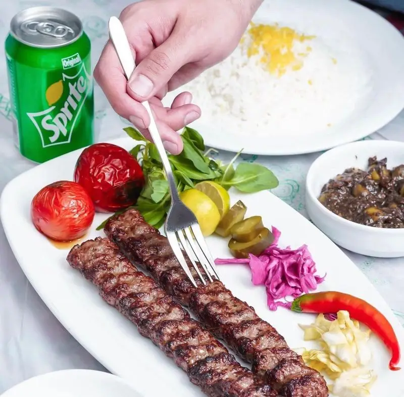 سرو کباب کوبیده اصیل ایرانی در رستوران الف. دو سیخ کوبیده آبدار با برنج زعفرانی، گوجه کبابی، لیمو و مخلفات ترش. لذت یک غذای خوشمزه.