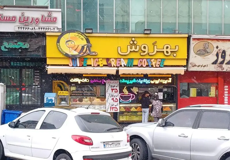 تابلوی زرد فروشگاه بستنی و آبمیوه بهروش شعبه جنت آباد، با لوگوی زنبور و نوشته JUICE ICE CREAM COFFEE در روز برفی.