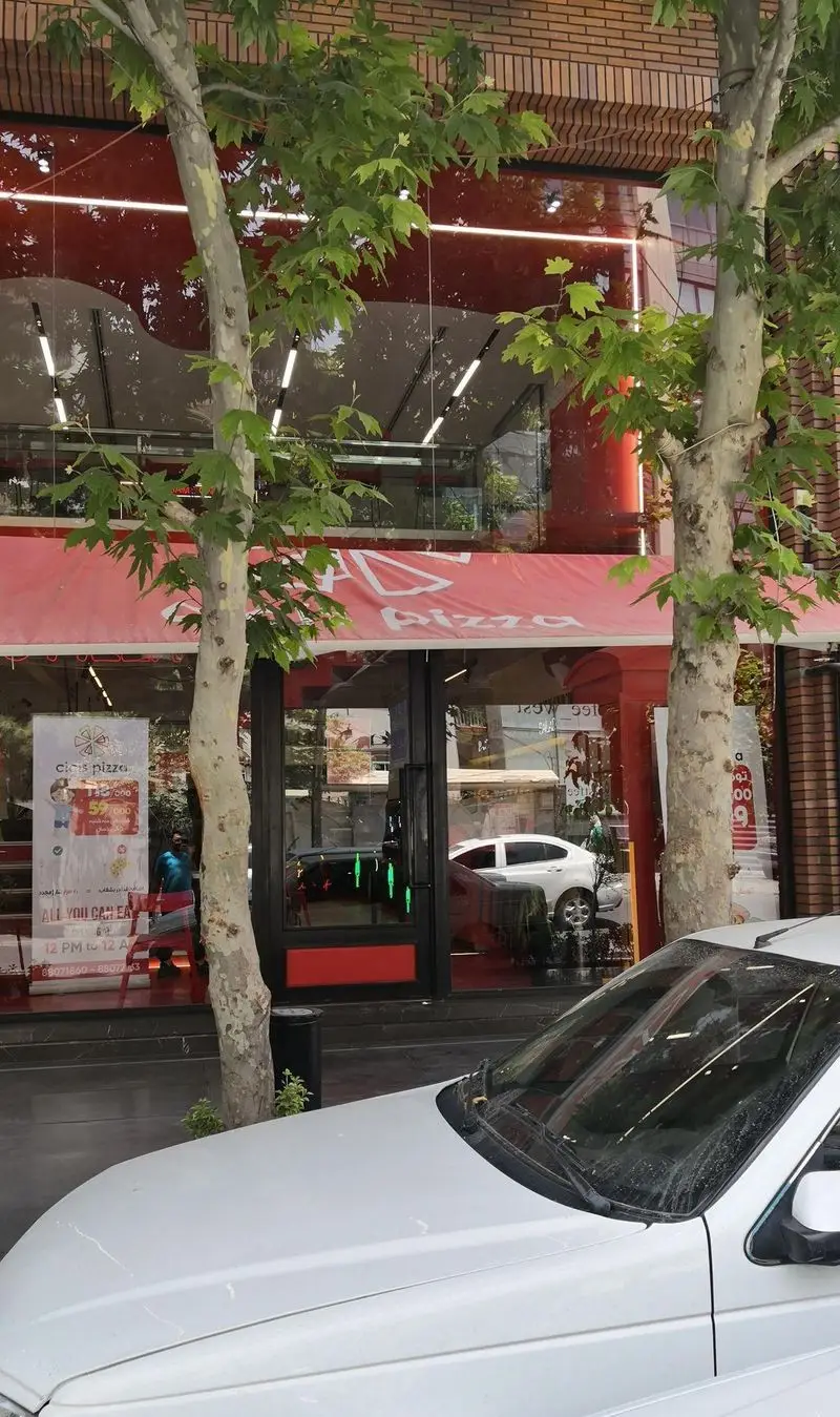 نمای بیرونی رستوران و فست فود پیتزا سیسیز، با طراحی مدرن شامل شیشه‌های بزرگ، سقف قرمز و درختان سبز کنار ورودی اصلی.