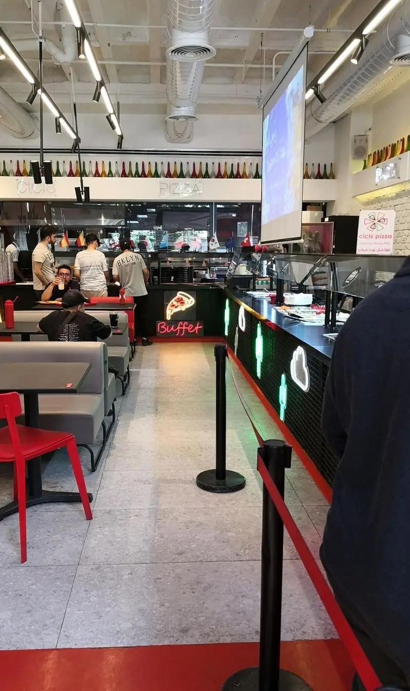 تصویر دکوراسیون داخلی رستوران پیتزا سیسیز، شامل بوفه سلف سرویس پیتزا و محل نشستن مشتریان در یک محیط مدرن و روشن. تجربه پیتزا.