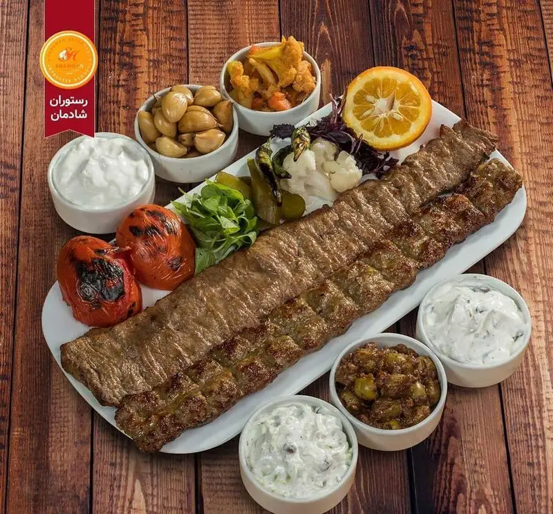 یک سینی کامل از غذای ایرانی رستوران شادمان: کباب کوبیده و برگ با گوجه کبابی، ماست و خیار، سیر ترشی و زیتون پرورده.