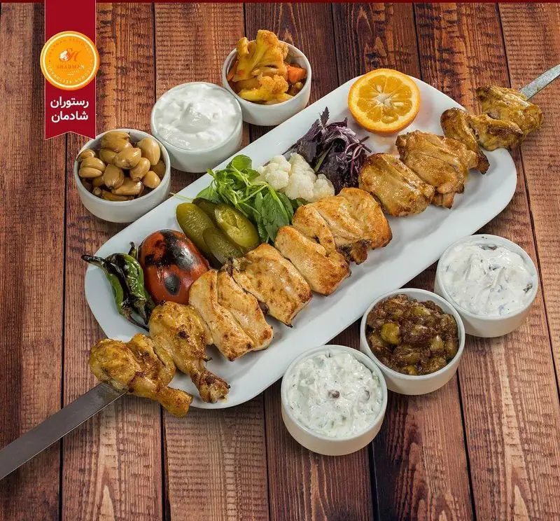 جوجه کباب لذیذ و مرغ کبابی رستوران شادمان، با سیر ترشی، گوجه، فلفل، خیارشور و سبزیجات تازه. غذای اصیل ایرانی.