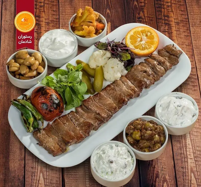 کباب گوشت لذیذ رستوران شادمان همراه با مخلفات سنتی ایرانی: ترشی، سیر ترشی، زیتون پرورده، ماست و سبزیجات تازه، تجربه‌ای دلپذیر.