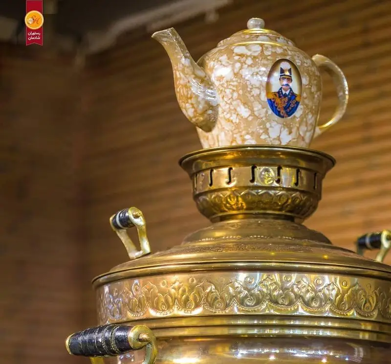 سماور و قوری سنتی با طرح‌های اصیل ایرانی و پرتره قاجاری، نمادی از فرهنگ چای در رستوران شادمان، فضایی دلنشین و نوستالژیک.