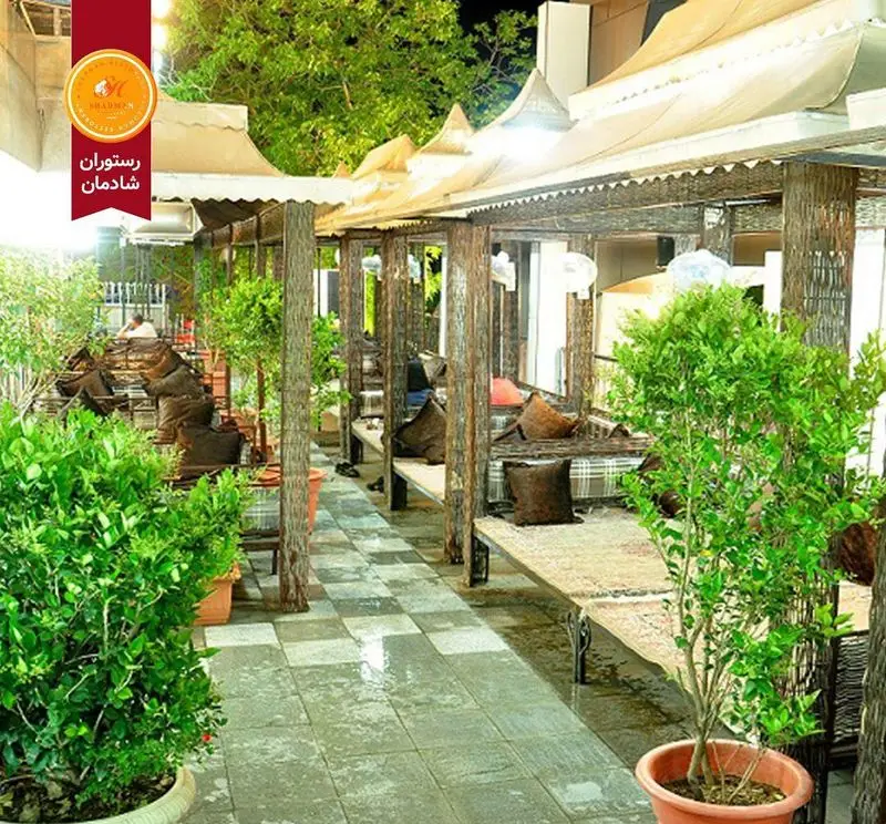 فضای باز رستوران شادمان با تخت‌های سنتی و محیطی سرسبز و دلنشین، ایده‌آل برای صرف غذا و دورهمی‌های خانوادگی در دل طبیعت.