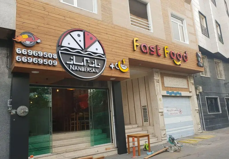 نمای بیرونی فست فود نانبرسان و کافه با تابلوی پیتزا، لوگوی ارسال غذا و شماره‌های تماس 66969508 و 66969509 برای سفارش آنلاین.