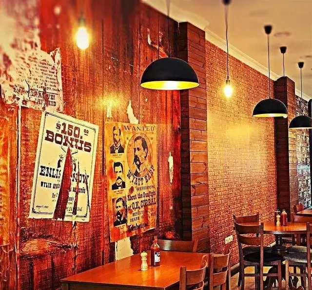 دکوراسیون داخلی رستوران نانبرسان با تم وسترن، دیوارهای چوبی و آجری، پوسترهای قدیمی و چراغ‌های آویز، فضایی گرم و دلنشین.