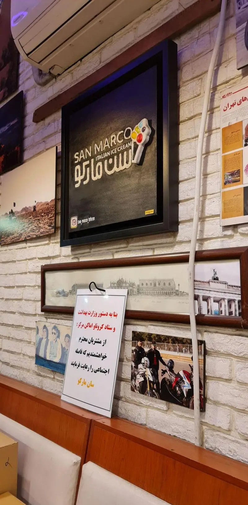 دکوراسیون داخلی بستنی فروشی سان مارکو با دیوار آجری، تابلوی بزرگ بستنی ایتالیایی و اطلاعیه رعایت فاصله اجتماعی.