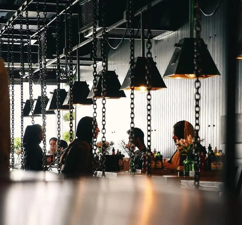 فضای داخلی جذاب و مدرن فست فود د ل پ با نورپردازی خاص، چراغ‌های زنجیری و مشتریان مشغول گفتگو و صرف غذا.