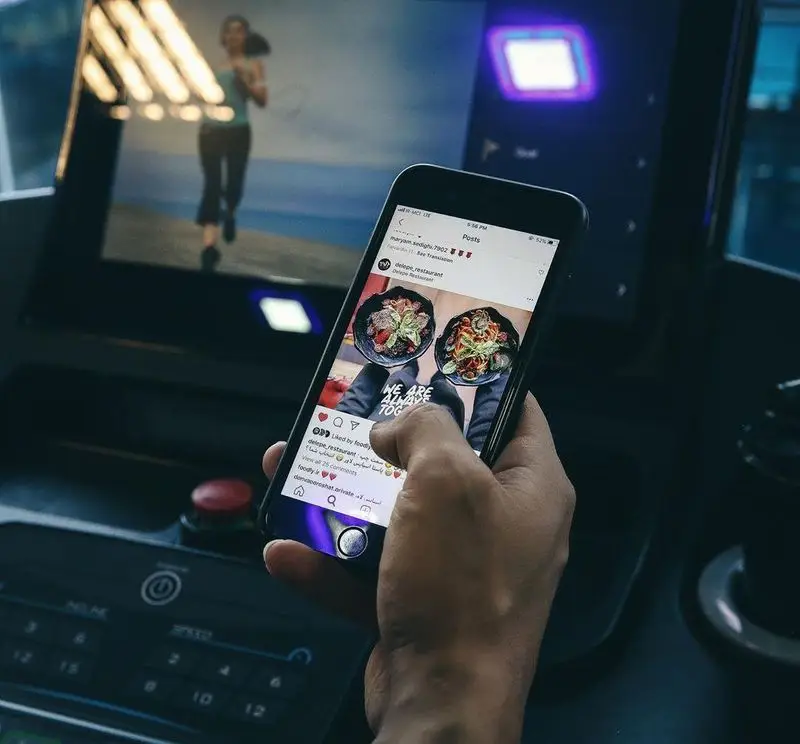 نمایش پست اینستاگرام رستوران فست فود د ل پ شامل غذاهای جذاب بر روی گوشی هوشمند، در حالی که در پس زمینه یک تردمیل دیده می شود.