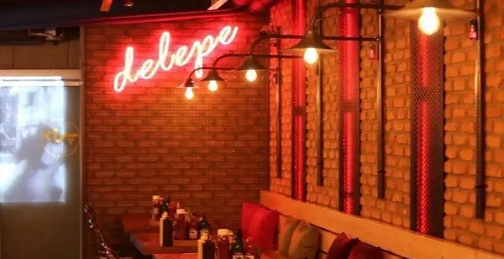 فضای داخلی شیک و مدرن فست فود د ل پ با دیوار آجری، نورپردازی جذاب، تابلو نئون Delepe و میزهای چوبی پر از سس.