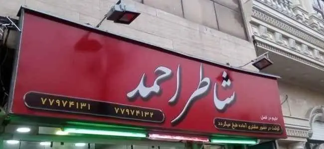 تابلوی قرمز رنگ کباب و حلیم شاطر احمد با شماره تلفن ۷۷۹۷۴۱۳۱ و ۷۷۹۷۴۱۳۲. گوشت تازه در حضور مشتری طبخ می‌شود.