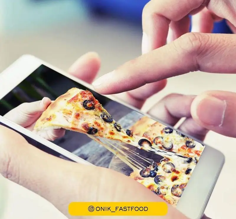مشتری در حال مشاهده و سفارش پیتزای محبوب و لذیذ فست فود اونیک با پنیر کشدار عالی از طریق صفحه موبایل.
