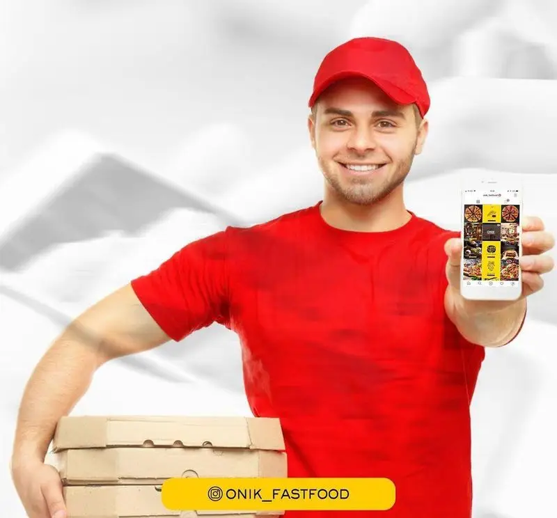 پیک خوشرو و آماده فست فود اونیک با لباس قرمز، جعبه‌های پیتزا را در دست دارد و اپلیکیشن موبایل سفارش آنلاین غذا را نمایش می‌دهد.