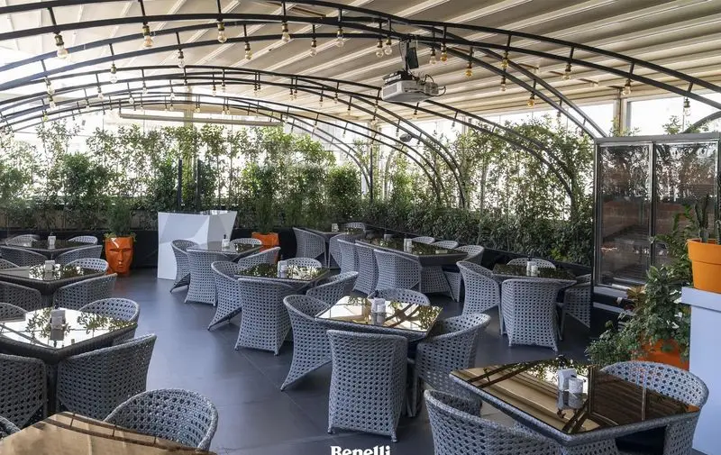 فضای روباز و دنج رستوران بنلی لانژ با میز و صندلی‌های حصیری، سقف سایبان، نورپردازی ملایم و دکوراسیون گیاهی شیک و مدرن.