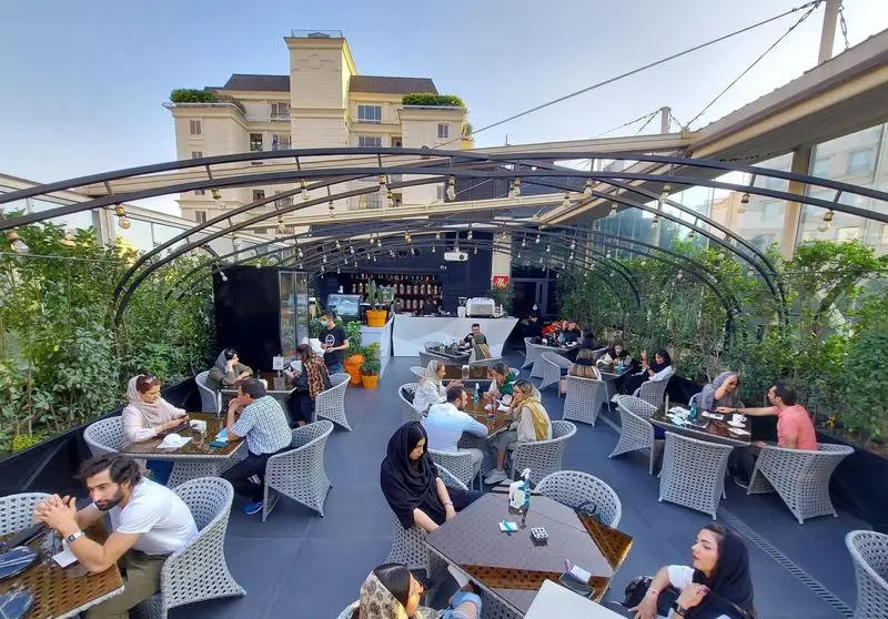 کافه رستوران بنلی لانژ: فضای باز دلنشین روف گاردن مدرن با طراحی شیک و مشتریانی در حال گپ و گفت در تهران.