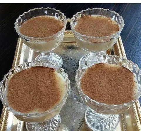 چهار کاسه دسر فرنی سنتی ایرانی با پودر دارچین روی سینی نقره‌ای، یک پایان دلنشین و شیرین در رستوران و سفره خانه دنج.