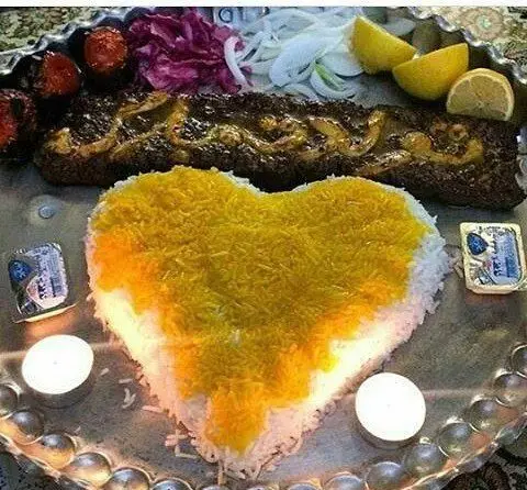غذای لذیذ ایرانی: کباب و برنج زعفرانی قلبی شکل با مخلفات در سینی نقره‌ای. شام رمانتیک در رستوران و سفره خانه سنتی دنج.