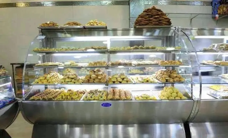 ویترین پر از انواع شیرینی‌های تازه و خوشمزه، از جمله شیرینی دانمارکی، کوکی، باقلوا و شیرینی‌های سنتی در قنادی.