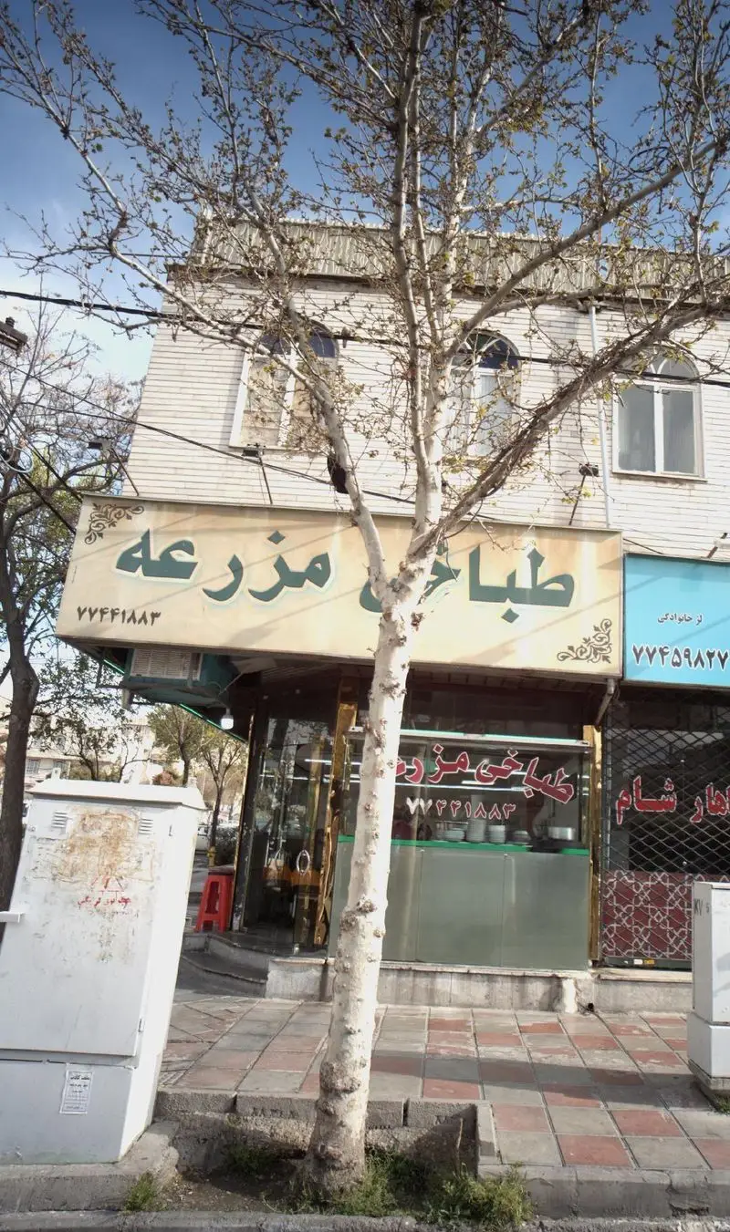 تصویر نمای جلوی طباخی مزرعه، یک رستوران سنتی ایرانی ارائه دهنده کله پاچه و غذاهای محلی، با تابلوی مشخص در کنار خیابان.