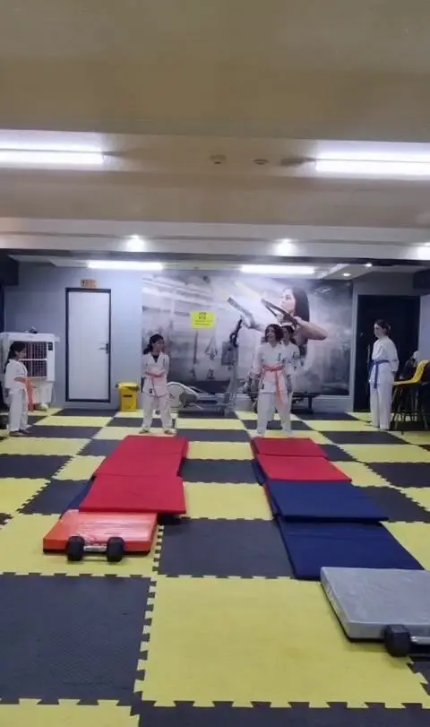 دختران و زنان در حال تمرین کاراته و هنرهای رزمی در باشگاه ورزشی گلایل، فضایی مجهز با تشک‌های تمرین برای تناسب اندام و ورزش.