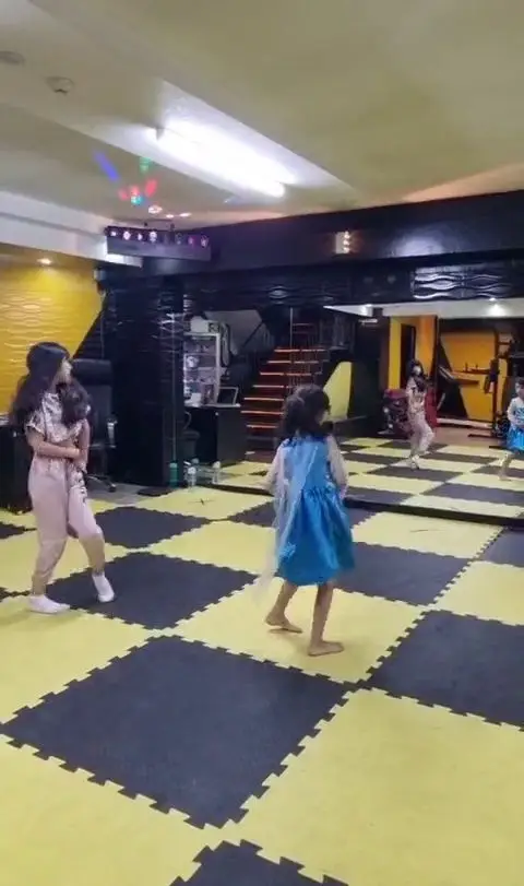 دختران در حال آموزش رقص و ورزش در باشگاه ورزشی گلایل با کف‌پوش شطرنجی و نورپردازی زیبا. مناسب کودکان و نوجوانان.