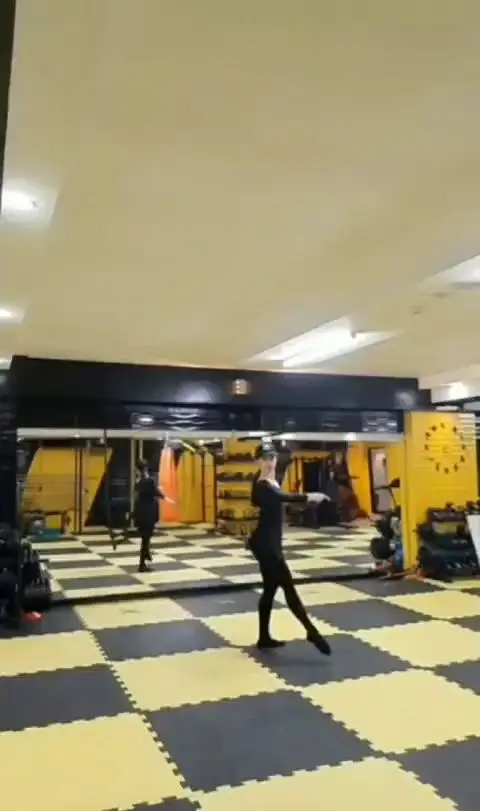 باشگاه ورزشی گلایل: زنی در حال انجام تمرینات رقص یا حرکات ورزشی در فضای مجهز باشگاه با کفپوش شطرنجی و آینه های بزرگ.