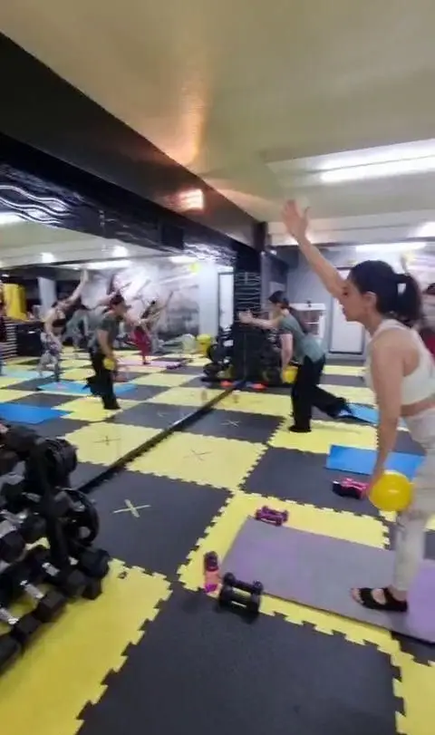 چند نفر در حال تمرین گروهی در محیط پویا و مجهز باشگاه ورزشی گلایل با کفپوش زرد و مشکی و تجهیزات فیتنس.