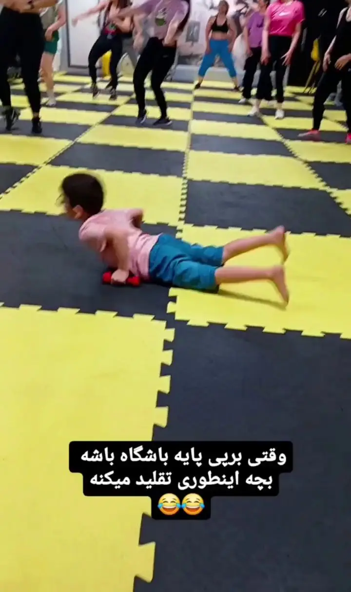 کودکی در باشگاه ورزشی گلایل در حال تقلید حرکات ورزشی بزرگسالان روی مت‌های زرد و سیاه، نشان‌دهنده محیط دوستانه و الهام‌بخش برای همه سنین.