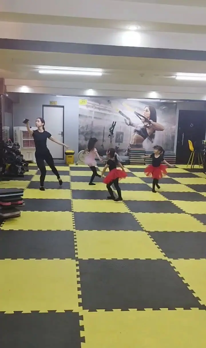 کلاس رقص و تناسب اندام کودکان در باشگاه ورزشی گلایل؛ مربی در حال آموزش رقص به دختران خردسال با لباس‌های رنگی در فضایی مدرن با کفپوش شطرنجی.