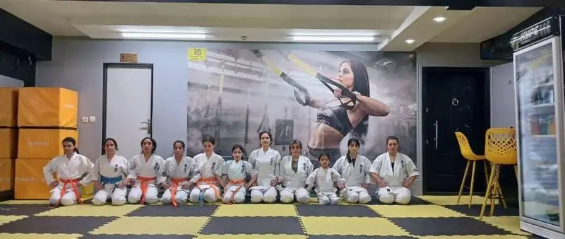 زنان و دختران کاراته کار باشگاه ورزشی گلایل در لباس فرم روی تشک نشسته اند. کلاس کاراته، هنرهای رزمی و آمادگی جسمانی.