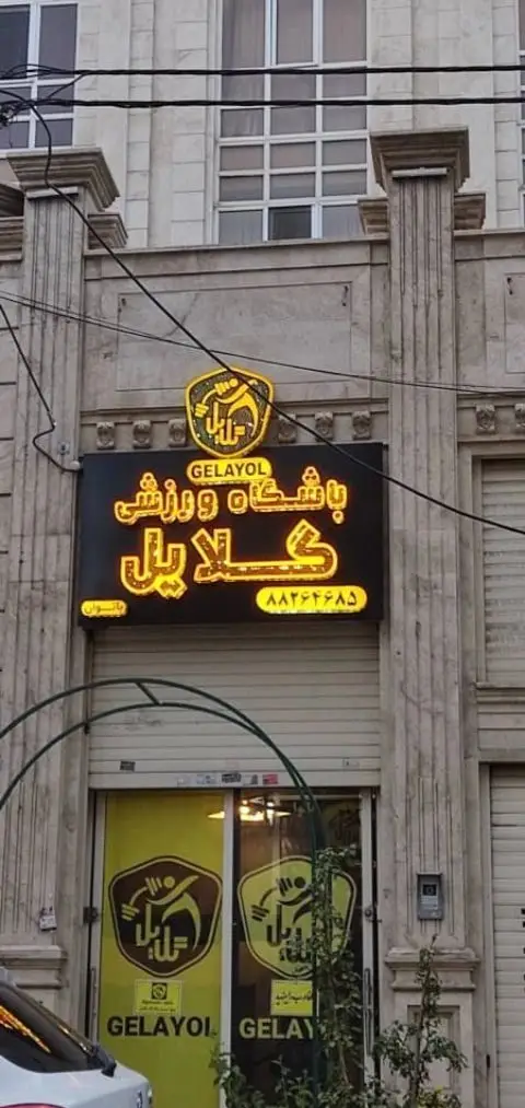 نمایی از باشگاه ورزشی گلایل، یک مرکز تناسب اندام با تابلوی نئونی بزرگ و لوگوی منحصربه‌فرد مرد وزنه‌بردار در ورودی.