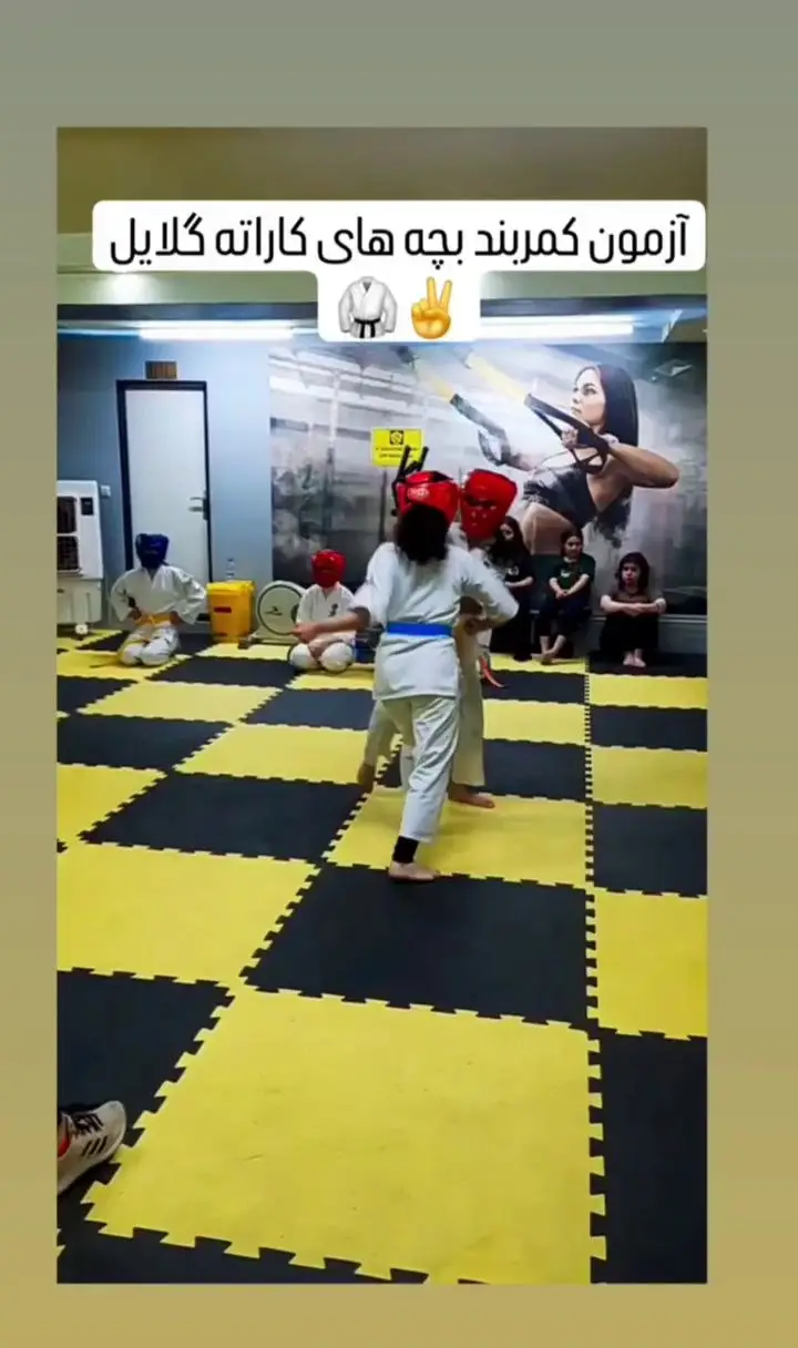 آزمون کمربند کاراته کودکان در باشگاه ورزشی گلایل. کودکان در حال نمایش مهارت‌های کاراته خود روی تشک‌های ورزشی زرد و مشکی هستند.