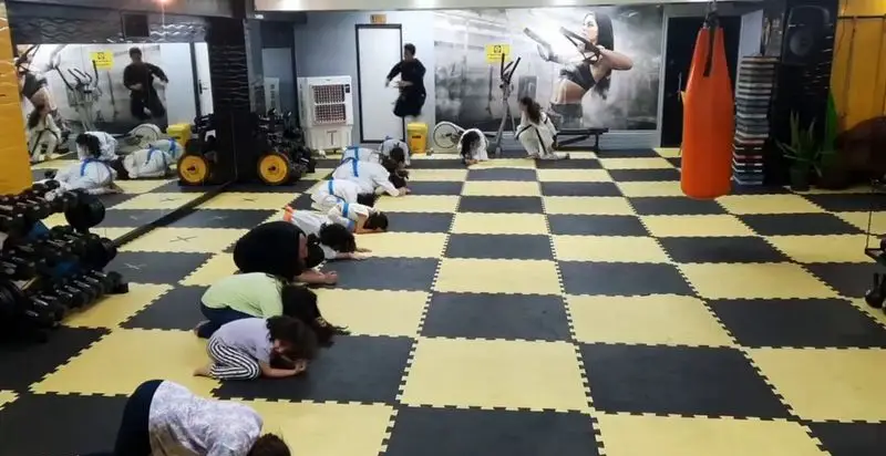 باشگاه ورزشی گلایل: هنرجویان هنرهای رزمی در حال ادای احترام روی تشک‌های شطرنجی زرد و مشکی. محیطی مناسب برای آموزش و تمرین آمادگی جسمانی.