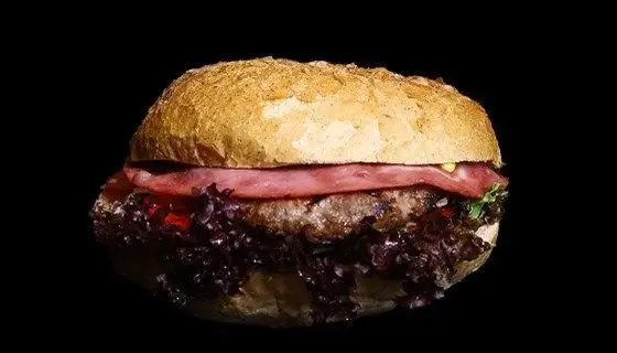 ساندویچ برگر لذیذ فست فود دیبارو با نان تازه، پتی گوشت گریل شده، ژامبون و کاهوی بنفش روی پس‌زمینه تیره.