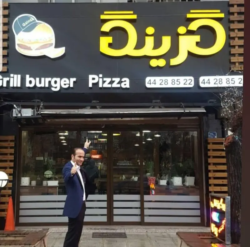 نمای بیرونی فست فود گزینگ برگر و پیتزا با تابلو نئون زرد، نمایش گریل برگر و پیتزا به همراه شماره تماس جهت سفارش غذا.