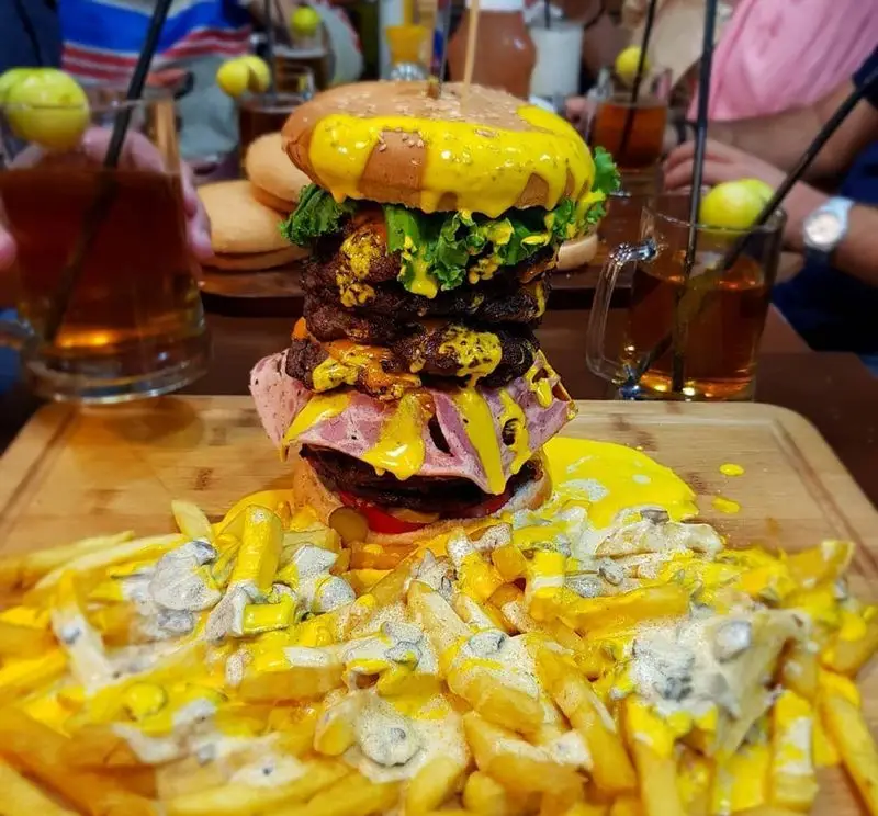 همبرگر غول‌آسای گزینگ برگر با لایه‌های متعدد گوشت، پنیر ذوب‌شده فراوان و کاهو در کنار سیب‌زمینی سرخ کرده پنیری و سس.
