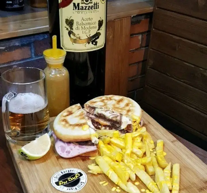 همبرگر خلاقانه گزینگ برگر برش‌خورده با سیب زمینی فراوان، سس مخصوص، نوشیدنی و برش لیمو روی تخته سرو چوبی جذاب.