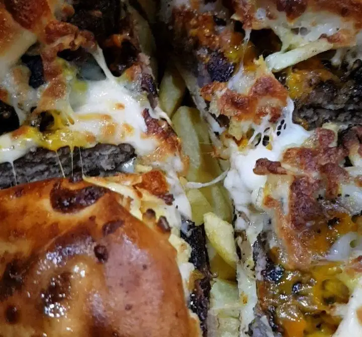 برگر نصف شده گزینگ برگر با پنیر فراوان آب شده، لایه‌های گوشت برگر و سیب‌زمینی سرخ شده طلایی در کنار آن.