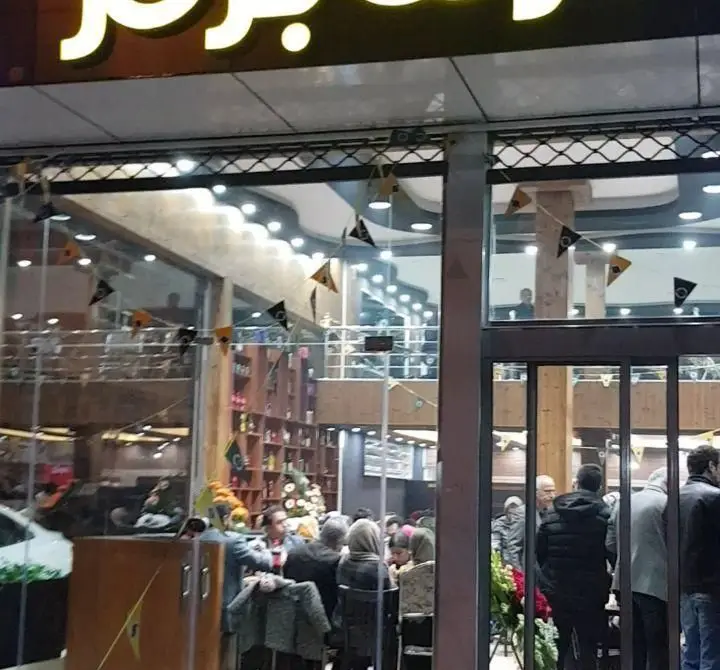 ورودی پر رفت و آمد شعبه گزینگ برگر، با مشتریان در حال انتظار و صرف غذا در فضای داخلی دو طبقه مدرن و نورپردازی جذاب