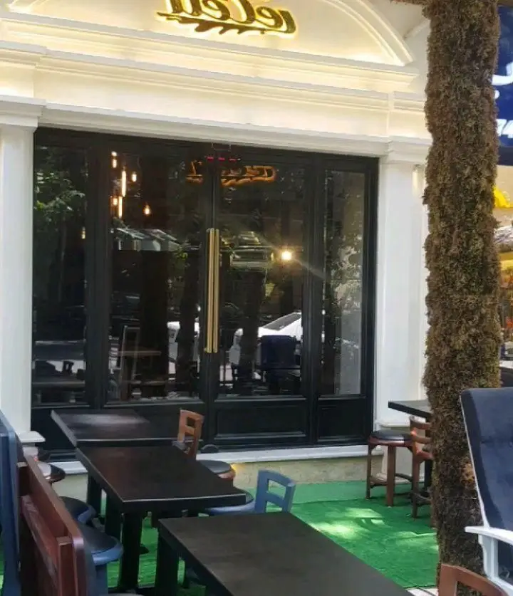 نمای بیرونی رستوران گزینگ برگر با فضای دنج نشیمن در فضای باز، میزهای چوبی تیره، صندلی‌های متنوع و ورودی مدرن.