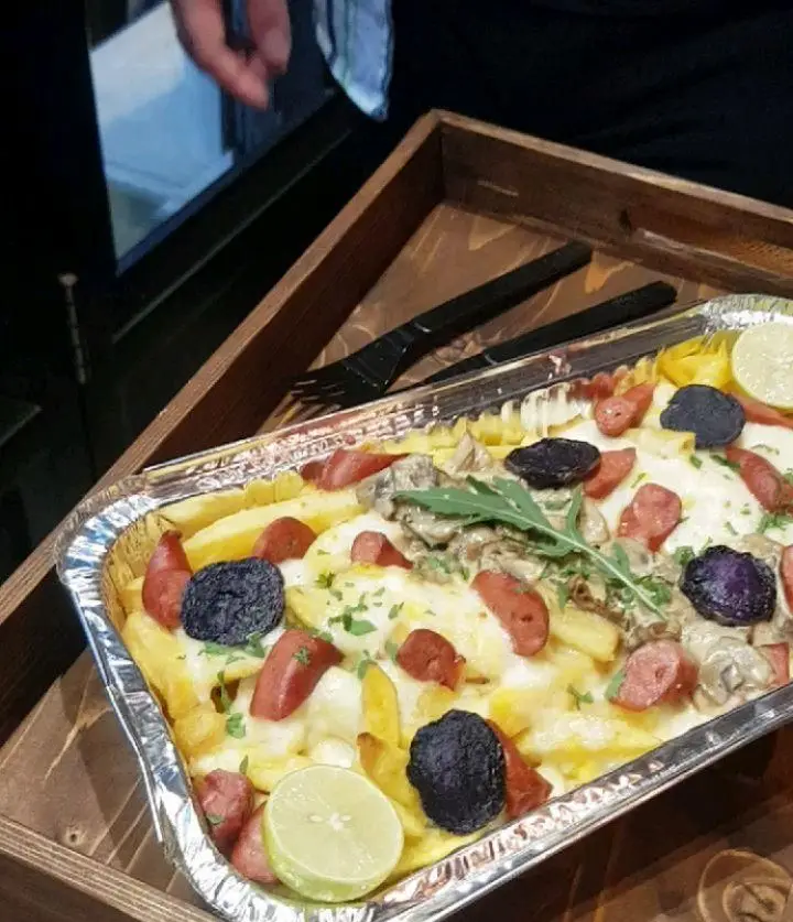 سیب‌زمینی سرخ‌کرده ویژه گزینگ برگر، با پنیر فراوان، سوسیس، قارچ، روکولا و لیمو. غذای فست فودی جذاب در ظرف آلومینیومی.