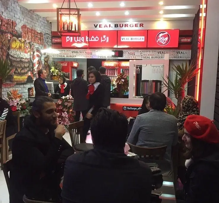 فضای داخلی شلوغ فست فود ویل برگر، با دکوراسیون جذاب، تابلوی برند ویل برگر و حضور مشتریان در حال لذت بردن از غذا.