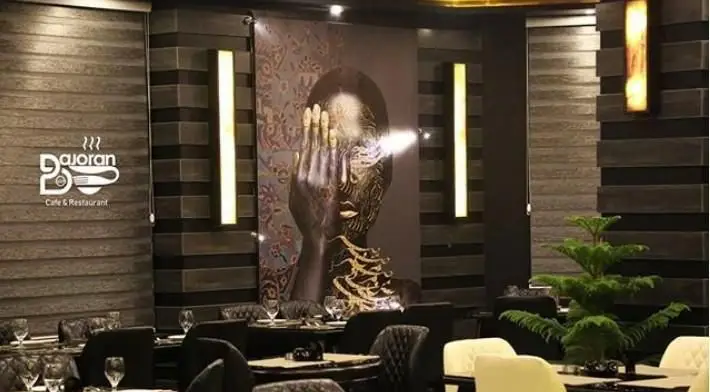 تصویری زیبا از فضای داخلی مدرن و دلنشین کافی شاپ و رستوران باژوران با دکوراسیون تیره، میزهای آماده و نورپردازی گرم.