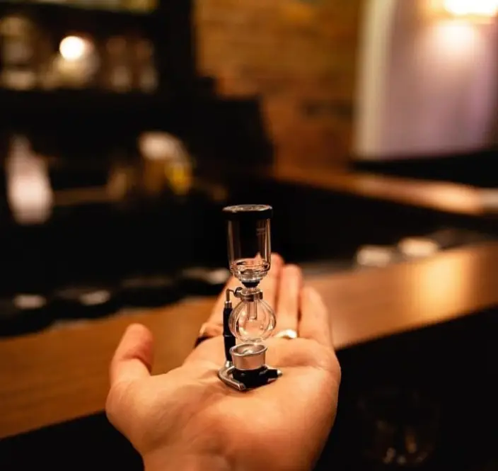 تصویری خاص از یک دستگاه قهوه ساز سایفون مینیاتوری در کف دست، نشان‌دهنده عشق به قهوه و دقت قهوه یویو در ارائه بهترین‌ها.