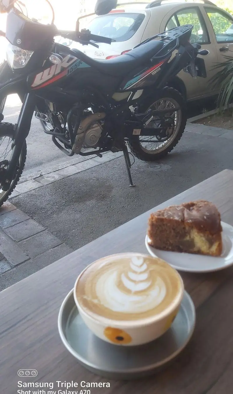 یک فنجان قهوه لاته آرت زیبا و یک برش کیک خوشمزه روی میز چوبی کافه قهوه یویو، با پس زمینه موتورسیکلت یاماها. لذت لحظات شما.